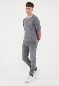 Maglione grigio a maniche lunghe con dettagli rosa, caratterizzato da un colletto e polsini a coste, abbinato a pantaloni slim grigi e sneakers bianche.