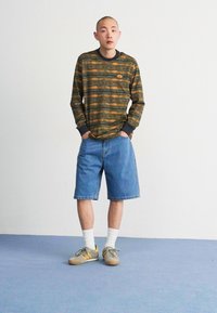 Long-sleeve shirt with green and orange horizontal stripes, paired with blue denim shorts, white socks, and gray sneakers with accents.