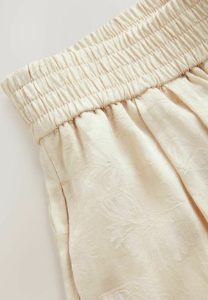 Cream-colored fabric with a textured floral pattern, featuring a smocked elastic waist and soft draping design.
