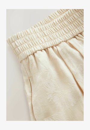 Krämfärgad tyg med ett strukturerat blommönster, med en smockad elastisk midja och mjuk draperad design.