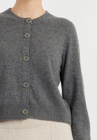 Cardigan grigio lavorato a maglia con scollo rotondo, sei bottoni frontali e orlo a coste. Il tessuto ha una consistenza morbida e un motivo sottile.