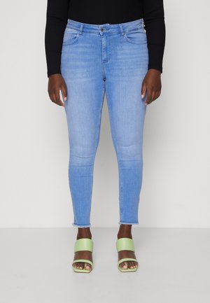 Light blue skinny jeans with a frayed hem, five-pocket design, and a smooth texture, paired with green block-heeled sandals.