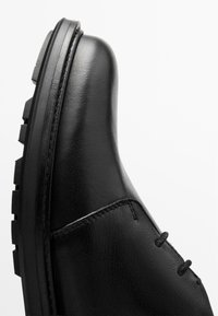 Bottines en cuir noir avec un bout arrondi, une tige texturée et une semelle en caoutchouc épaisse et striée, ornée de détails de couture subtils.