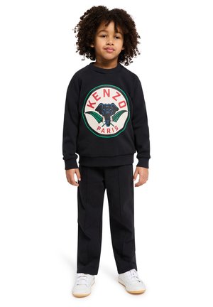 Zwarte crewneck sweatshirt met een cirkelvormige graphic van een olifant en "KENZO PARIS," gecombineerd met zwarte broeken. Witte sneakers.