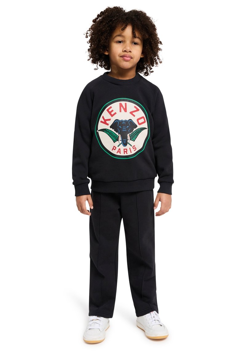 Sweatshirt noir à col rond avec un graphique circulaire représentant un éléphant et "KENZO PARIS", associé à un pantalon noir. Baskets blanches.
