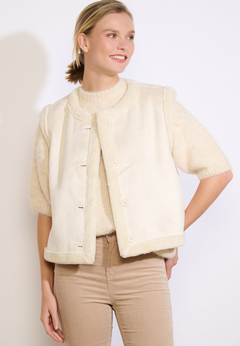 Crème-kleurige mouwloze vest, gemaakt van zachte faux bont met een gestructureerde afwerking, met een ronde kraag en vier knoopsluitingen.