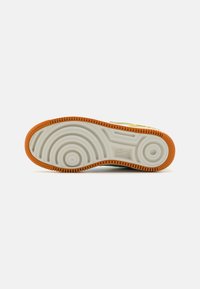 Semelle de sneaker Nike avec un motif circulaire, en caoutchouc blanc texturé, et une semelle orange. Logo Nike en relief.