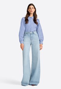 Chemise à rayures bleues et blanches avec des manches bouffantes, assortie à un jean large bleu clair. Les deux vêtements présentent des designs décontractés et ajustés.