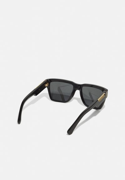 Ochelari de soare negri cu ramă pătrată, lentile fumurii gri și accente aurii pe brațe. Material din plastic lucios.