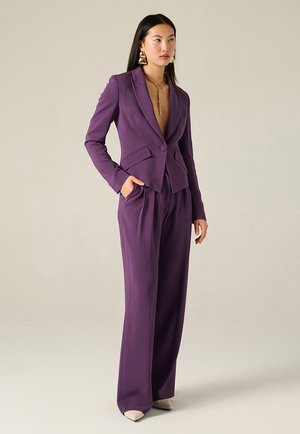 Blazer viola su misura con scollo a V profondo, due tasche frontali e chiusura con un bottone, abbinato a pantaloni a vita alta e gamba ampia.