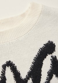 Maglione lavorato a maglia con una base bianca e un spesso motivo ricamato in nero. Il colletto a coste e la texture migliorano la profondità visiva.