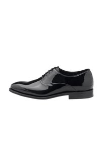 Chaussure de ville en cuir verni noir avec une surface lisse et brillante, à lacets à l'avant, à bout effilé et à talon bas et plat.