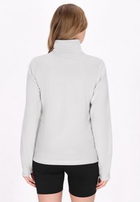 Lys grå, langærmet fleece-top med høj krave, glat struktur og flade sømme; parret med sorte shorts.