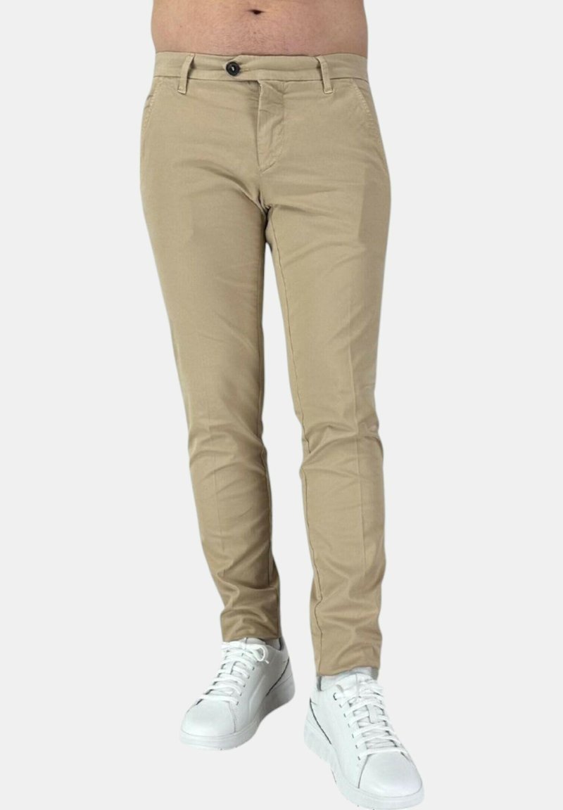 Chino beige su misura con vestibilità slim, dotati di chiusura a bottone e abbinati a sneakers bianche. Texture liscia, senza motivi visibili.