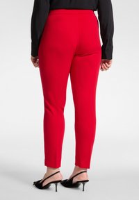 Czerwone dopasowane spodnie o gładkiej fakturze, z krótką nogawką i wysokim stanem. Połączone z czarnymi sandałami na obcasie ze smukłym paskiem i spiczastym noskiem.