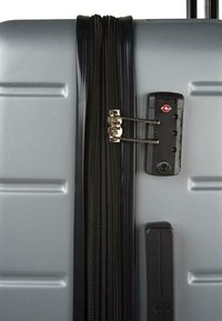 Maleta rígida plateada con textura acanalada vertical, cerradura y cremalleras negras, cuenta con cerradura aprobada por la TSA, mango resistente y acentos.