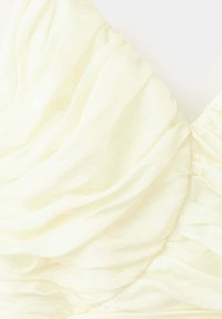 Gros plan d'un tissu de couleur crème avec des plis doux et froncés créant une texture froncée sur un matériau léger.