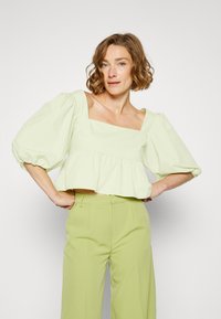 Top crop verde menta com decote quadrado, mangas bufantes e bainha com babados, combinado com calças largas verde claro feitas de tecido suave.
