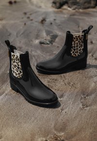 Botas de tobillo de goma negra con un panel lateral elástico de estampado de leopardo, suela texturizada y lengüetas de tiro. Acabado suave y diseño de punta redonda.