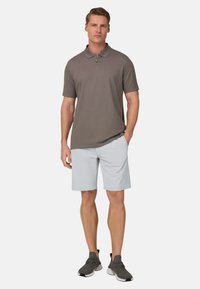 Graues Poloshirt mit kurzen Ärmeln und einem Reißverschluss, kombiniert mit hellgrauen Shorts. Das Modell trägt dunkelgraue Sneakers und steht in einer neutralen Pose.