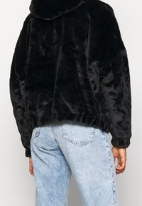 Sort faux fur cropped jakke med hætte, ribbet kant og afslappet pasform, parret med lys blå straight-leg jeans.