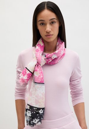 Giovane donna con capelli lisci e scuri indossa una maglia rosa a maniche lunghe e una sciarpa floreale rosa, bianca e nera annodata intorno al collo.