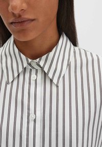 Weißes und braun gestreiftes Hemd mit klassischem Kragen, ausgestattet mit Knopfverschlüssen und einer glatten Stoffstruktur. Details umfassen zwei Knöpfe am Kragen.