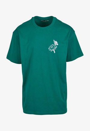 Turkusowa bawełniana koszulka z grafika białego kwiatu i motyla po lewej stronie. Krótkie rękawy i okrągły dekolt.