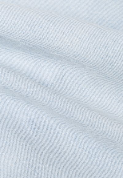 Vaaleansininen farkkukangas, jossa on hieno twill-sidos, joka tuo esiin hienovaraisen tekstuurin ja vinot viivat sekä näkyvät taitteet ja laskokset.