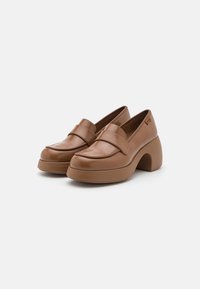 Paire de mocassins à plateforme en cuir marron avec bouts arrondis et talons carrés sur fond blanc.
