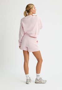 Completo felpa e pantaloni corti rosa chiaro, con una vestibilità rilassata, polsini a costine e una texture liscia, abbinato a scarpe da corsa argentate.