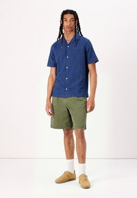 Short-sleeve navy button-up shirt, olive green shorts, tan sneakers, and white socks. The shirt features a collar and two front pockets.