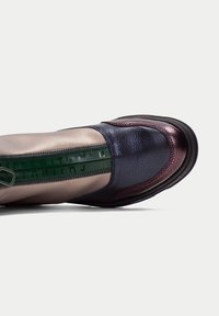 Zapato multicolor con una mezcla de cuero metálico bronce, azul profundo y burdeos. Presenta una cremallera verde y un detalle texturizado en la puntera.