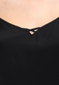 Svart topp med v-hals och dekorativ korsbandning fram. Slätt, lättviktsmaterial.