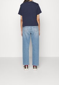Camiseta corta de color azul marino, jeans de pierna ancha de color azul claro, zapatillas blancas con acentos rojos y negros. Vista desde detrás, mostrando el ajuste y el diseño.