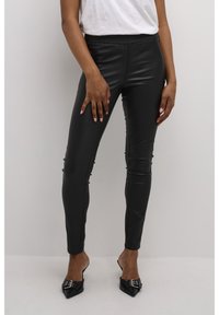 Czarne legginsy z ekologicznej skóry o dopasowanym kroju, z wysokim elastycznym paskiem i bocznymi zdobieniami. Noszone z czarnymi szpilkami z noskiem w szpic.