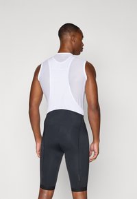 Vêtements de sport pour hommes comprenant un débardeur en mesh blanc sans manches et un short noir ajusté, avec des coutures contrastées et une texture lisse.