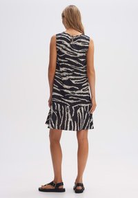 Ärmelloses schwarzes Kleid mit einem weißen Tigerstreifenmuster, mit einem ausgestellten Saum und einem Schlüsselloch-Detail im Rücken. Leichter, glatter Stoff.