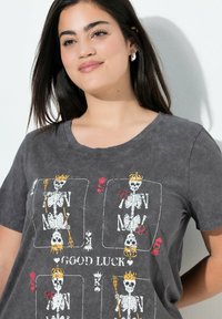 Camiseta de algodón gris con un estampado gráfico de esqueletos con coronas y rosas, acentuada con detalles en rojo y amarillo, cuello redondo.