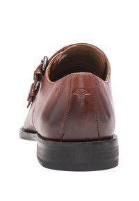 Chaussure habillée en cuir marron avec une sangle à boucle sur le côté, couture au dos, détail de logo en relief, et semelle noire vue de l'arrière.