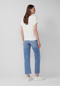 Witte t-shirt met korte mouwen, gecombineerd met lichtblauwe rechte jeans en zilveren sneakers. Eenvoudig ontwerp, zachte textuur, casual pasvorm.