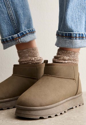 Botines de ante marrón con acabado texturizado, con puntera redonda y suela gruesa con dibujo. Combinados con cómodos calcetines beige de canalé.