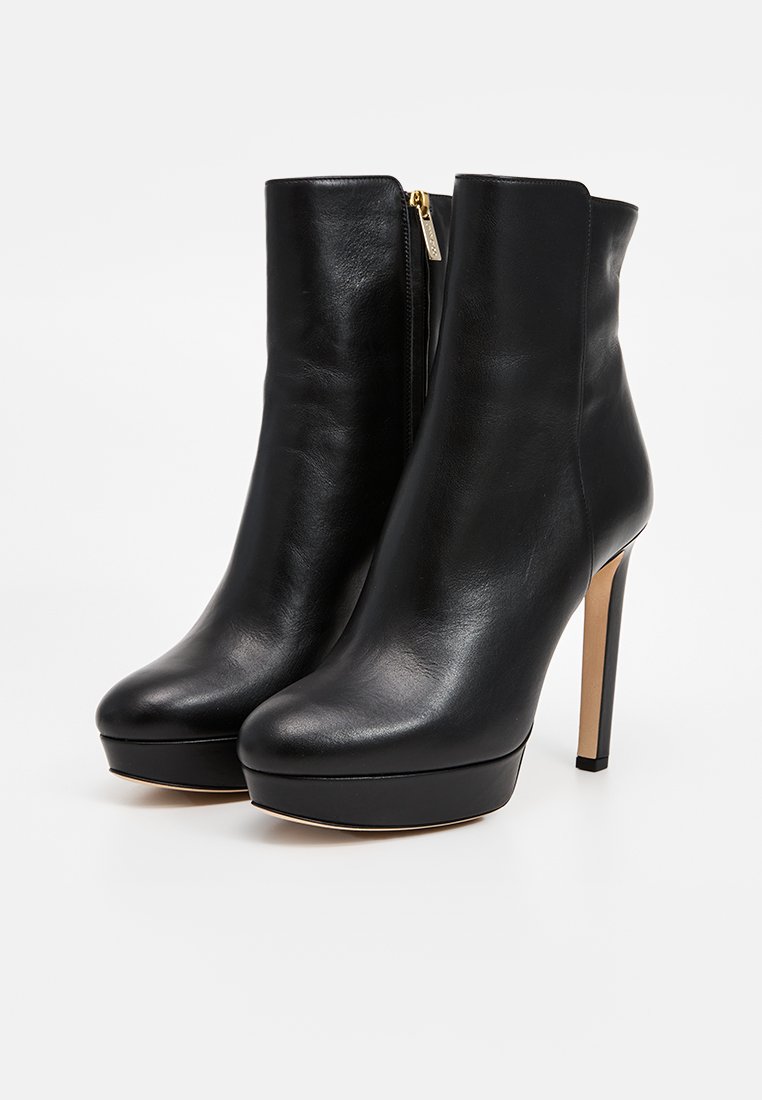 Bottines en cuir noir avec un talon haut, semelle à plateforme et fermeture éclair sur le côté. Texture lisse, bout arrondi et silhouette élégante.