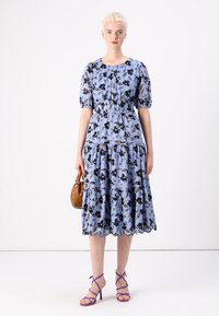 Lys blå kjole med blomsterprint, korte pufferm, elastisk midje, lagdelt skjørt, bølget kant, sammen med lilla stroppestøvel og brun veske.