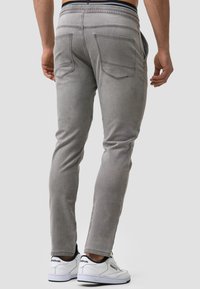 Pantalones gris ajustados con textura de denim, cinturilla elástica y bolsillos traseros prominentes. Combinados con zapatillas blancas con acentos negros.