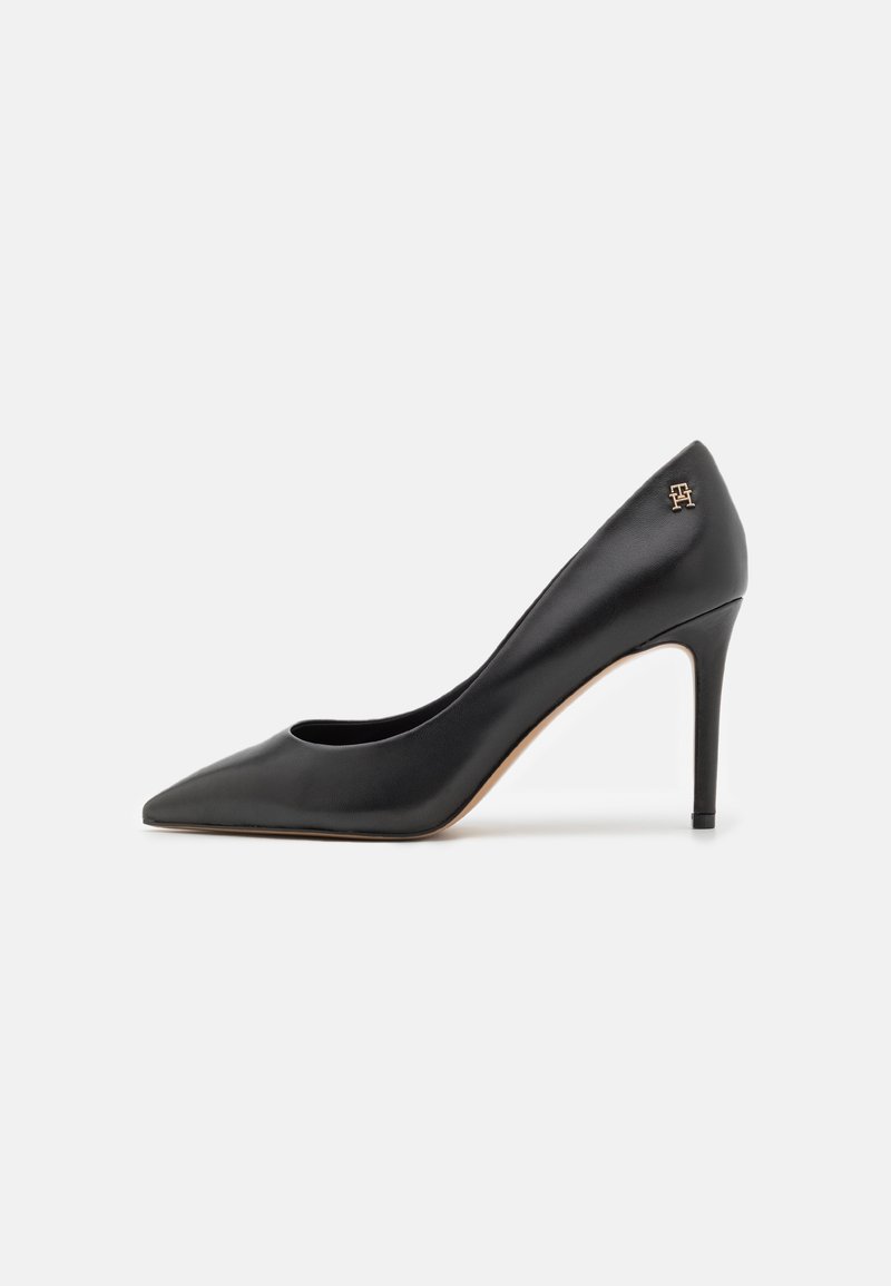 Escarpin en cuir noir à bout pointu avec talon aiguille fin et petit logo doré de la marque près de la cheville.