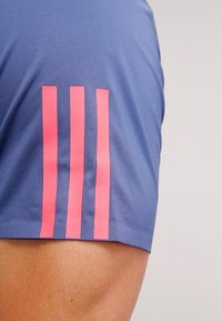 Camiseta deportiva de manga corta en tejido azul claro con tres rayas verticales rosas en la manga izquierda. Textura suave, diseño ajustado.