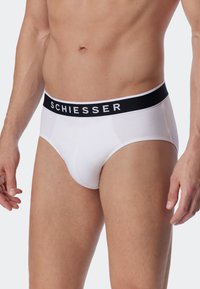 Slip in cotone bianco con fascia elastica nera recante la scritta "SCHIESSER". Texture liscia e design tradizionale dei slip.
