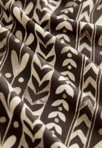 Brunt mønstrede stof med hvide botaniske designs, der viser blade og prikker, samtidig med at det yder en glat tekstur og intrikate designelementer.