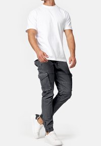 White crew neck t-shirt paired with dark gray cargo pants featuring multiple pockets and elastic cuffs, worn with white sneakers.